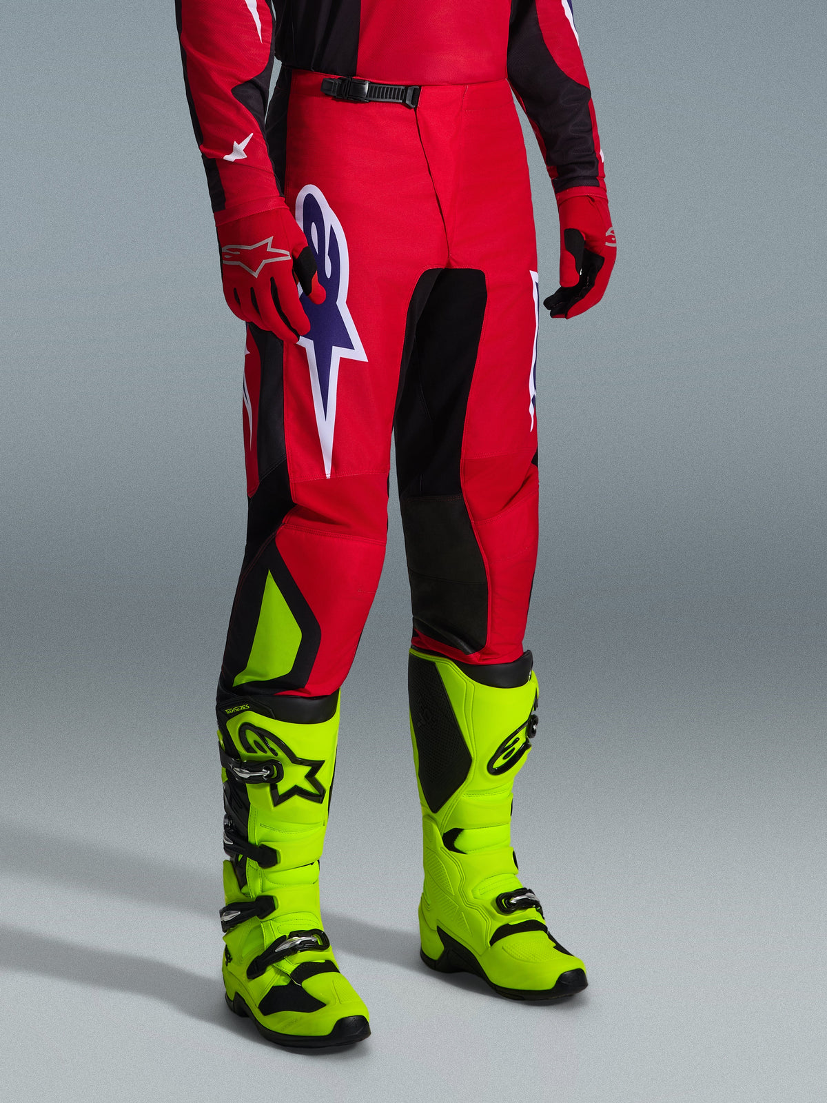 Alpinestars 2026 Fluid Grid Hose, Motocross-Hose, Rot, Schwarz und Lila, getragen mit neongelben Stiefeln und roten Handschuhen, mit schwarzen Paneelen und einem großen lila-weißen Stern-Logo, strapazierfähiges Sport-Fit-Design für Offroad-Rennen