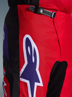 Alpinestars 2026 Fluid Grid Hose, Motocross-Hose, Rot, Schwarz und Lila, Nahaufnahme des Taillen- und Hüftbereichs mit einem schwarzen Ratschenverschluss und einem großen lila Alpinestars-Sternlogo mit weißer Umrandung, strapazierfähiges strukturiertes Gewebe für den Offroad-Rennsport.