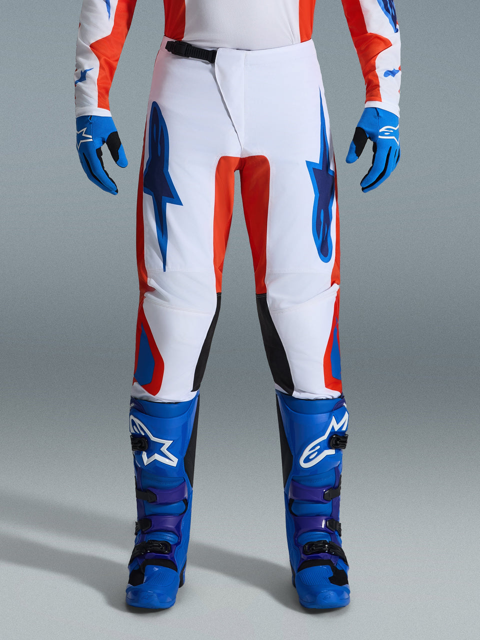Alpinestars 2026 Fluid Grid Hose, Motocross-Hose, Orange und UCLA Blau, getragen mit passenden blauen Stiefeln und Handschuhen, weißes Chassis mit markanten blauen Logos und orangefarbenen Akzenten, ergonomisches Design für Offroad-Performance