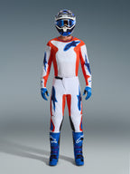 Motocross-Fahrer in kompletter Rennausrüstung, Alpinestars 2026 Fluid Grid Hose in Orange und UCLA Blau, weißes Trikot mit orangen Ärmeln und blauen Logos, passender blauer Helm und Brille, blaue Stiefel und blaue Handschuhe, abgestimmtes Outfit für Offroad-Rennsport