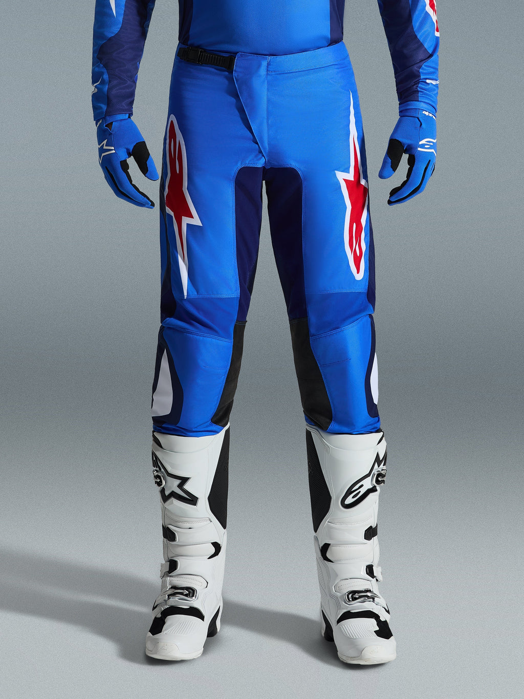 Alpinestars 2026 Fluid Grid Hose, Motocross-Hose, Blau und Rot, mit markanten roten und weißen Stern-Logos auf den Oberschenkeln, kombiniert mit passenden blauen Handschuhen und weißen Offroad-Stiefeln, sportliche Passform mit strapazierfähigen Einsätzen für den Rennsport.