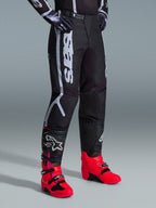 Alpinestars 2026 Fluid Apex Hose, Motocross-Hose, Schwarz und Grau, getragen mit leuchtend pinkfarbenen und roten Stiefeln sowie passendem schwarz-weißem Trikot, mit markantem vertikalem Alpinestars-Schriftzug am Oberschenkel, verstärkten Einsätzen und Ratschenverschluss für optimale Offroad-Performance.