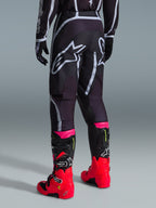 Alpinestars 2026 Fluid Apex Hose, Motocross-Hose, Schwarz und Grau, Rückansicht mit großen weißen Alpinestars-Logos am Gesäß, kombiniert mit leuchtend roten und pinken Stiefeln, strapazierfähige 600D-Polygewebe-Konstruktion für Offroad-Performance