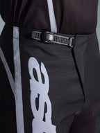 Alpinestars 2026 Fluid Apex Hose, Motocross-Hose, Schwarz und Grau, Nahaufnahme des integrierten Ratschenverschluss-Systems für eine sichere Passform, mit weißen Logo-Grafiken auf strapazierfähigem 600D-Polygewebe.
