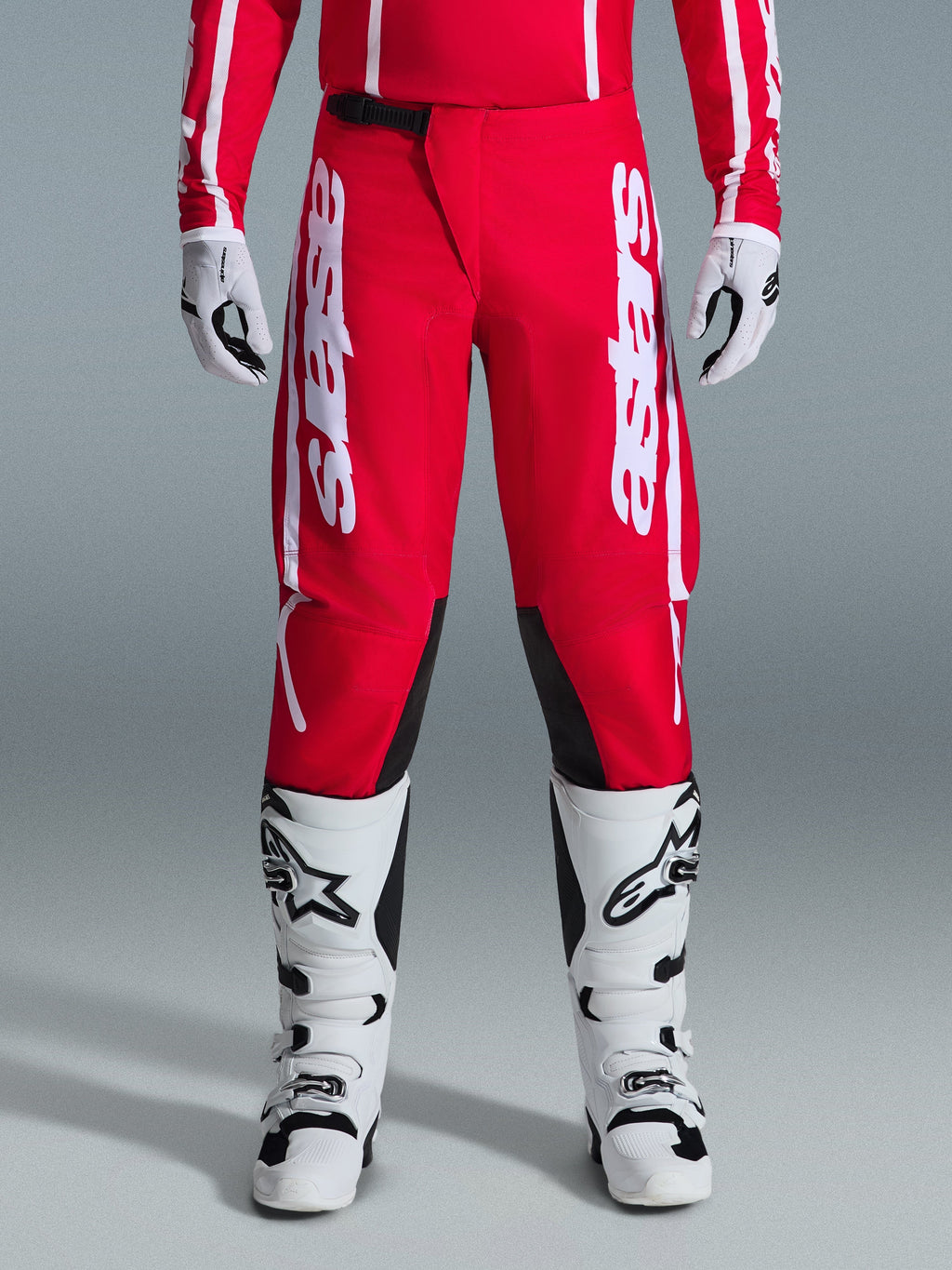 Alpinestars 2026 Fluid Apex Hose, Motocross-Hose, Rot und Weiß, mit großen weißen Astars-Logos auf den Oberschenkeln und schwarzen Knie-Innenpaneelen, getragen mit passenden weiß-schwarzen Stiefeln und Handschuhen für einen kompletten Offroad-Racing-Look.