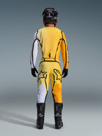 Alpinestars 2026 Fluid Apex Pants, Motocross Pants, Yellow and Black, rear view of a rider in full motocross gear, matching jersey with white and orange gradients, black helmet, black boots, and black gloves, coordinated off-road outfit.