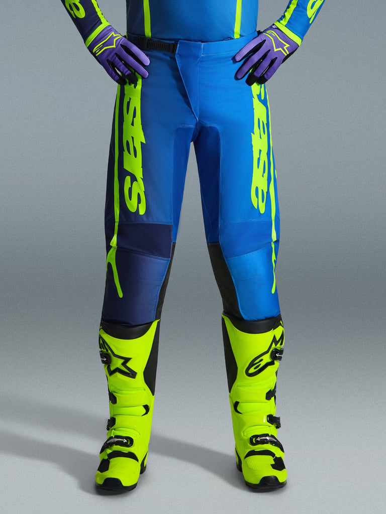 Alpinestars 2026 Fluid Apex Hose, Motocross-Hose, Blau und Gelb Fluo, kombiniert mit passenden neongelben Stiefeln und lila Handschuhen, markantes gelbes Branding an den Seiten, ergonomisches Design für Offroad-Rennsport