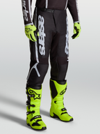 Alpinestars Fluid Apex V2 Pants, Men’s Motocross Gear in Black and Silver, featuring Alpinestars branding and durable 600D polyfabric. Shown on-model with bright yellow boots.