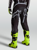 Alpinestars Fluid Apex V2 Pants, Black and Silver motocross pants for men shown on a rider with fluorescent yellow boots.