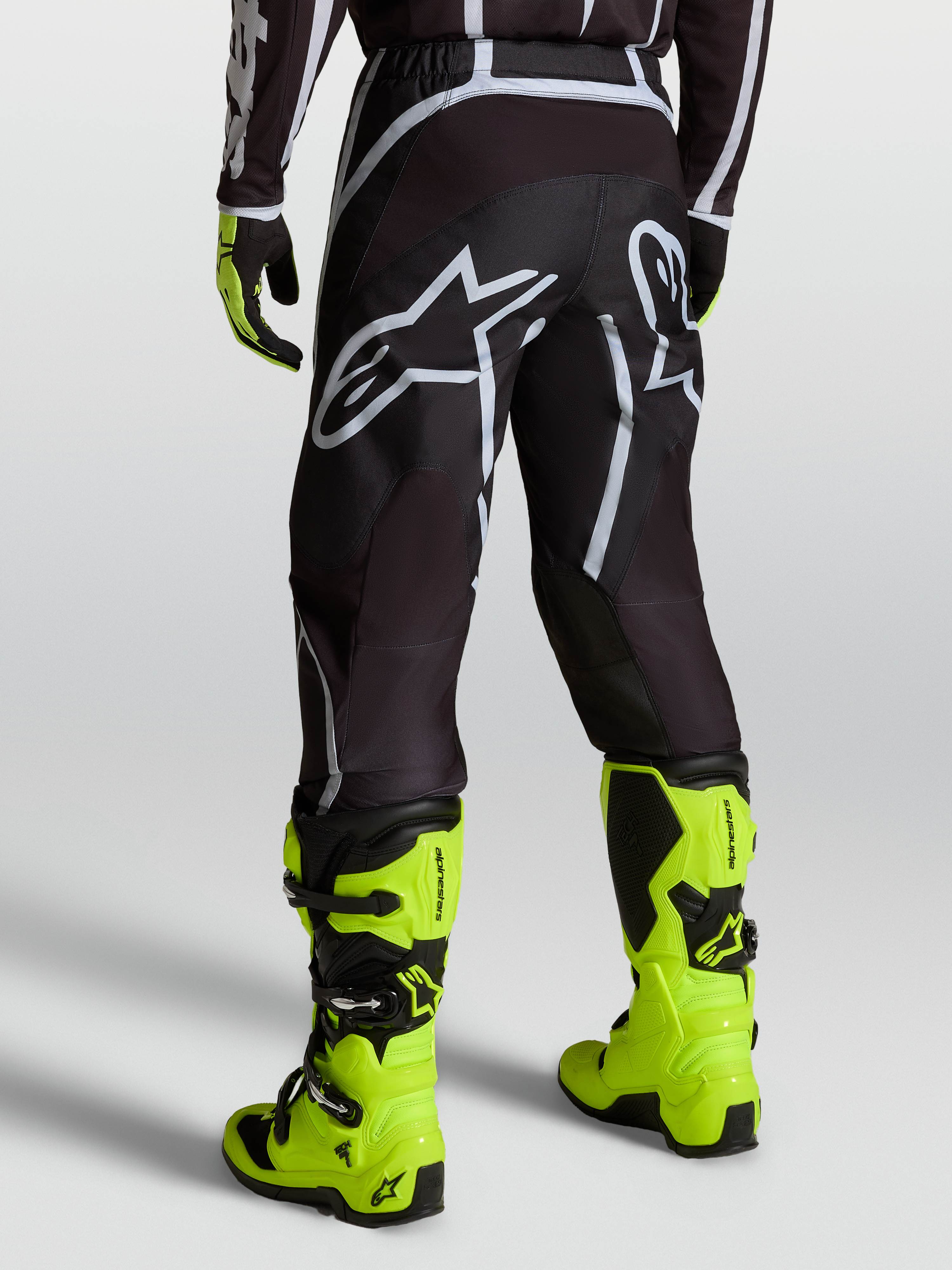 Alpinestars Fluid Apex V2 Pants, Black and Silver motocross pants for men shown on a rider with fluorescent yellow boots.