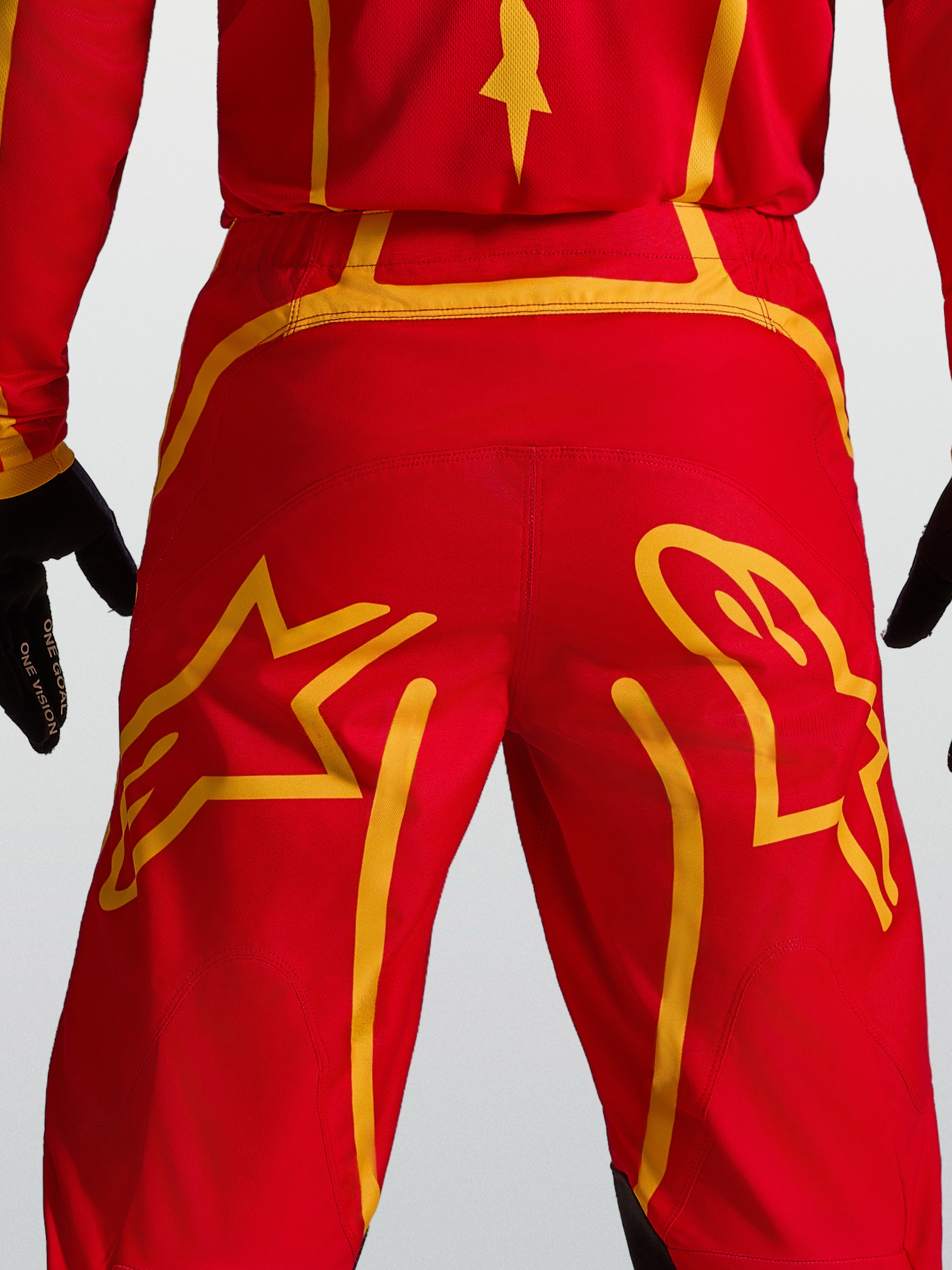 Alpinestars Fluid Apex V2 Hose, Motocross-Ausrüstung in Rot und Gold, mit verstärktem Rückenkoller und Stern-Grafiken.