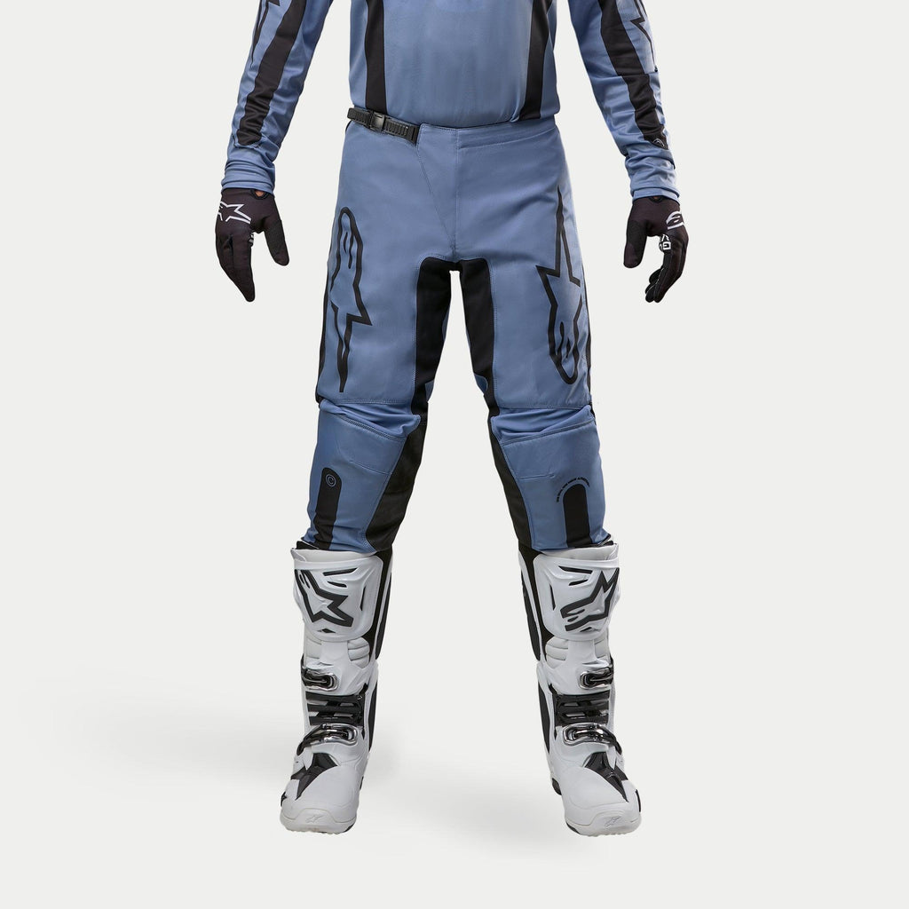 Alpinestars 2024 Fluid Lurv Hose, Motocross-Hose, Hellblau und Schwarz, getragen mit weißen und schwarzen Rennstiefeln und passenden Handschuhen, mit markanten schwarzen Stern-Logos auf den Oberschenkeln, ergonomisches Design für Offroad-Performance
