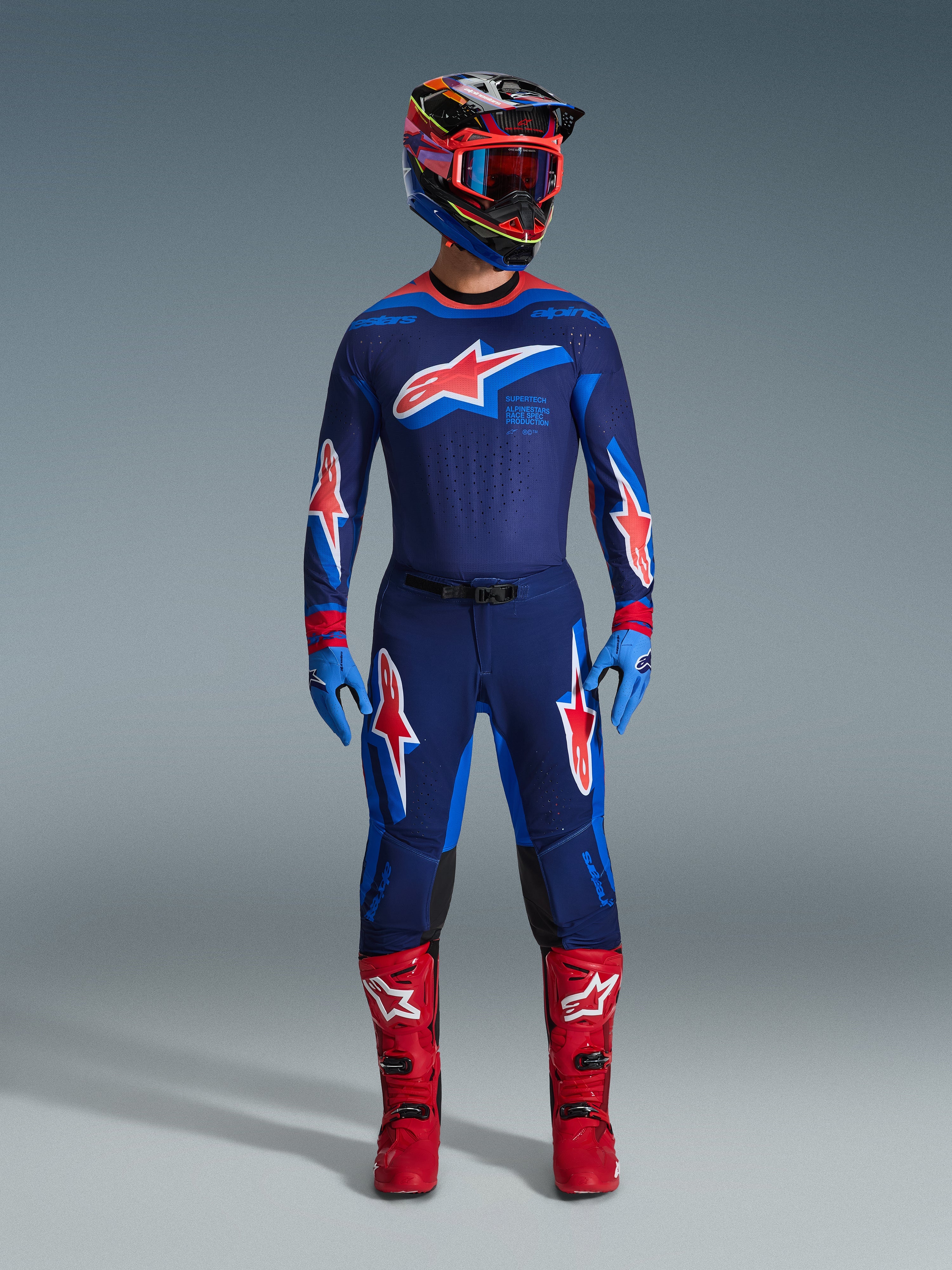 2026 Supertech Vista Gear Set, complete motocross racing outfit, dark blue jersey and pants featuring red and white star logos, multicolored helmet with red goggles, light blue gloves, and bright red boots, professional-grade MX gear