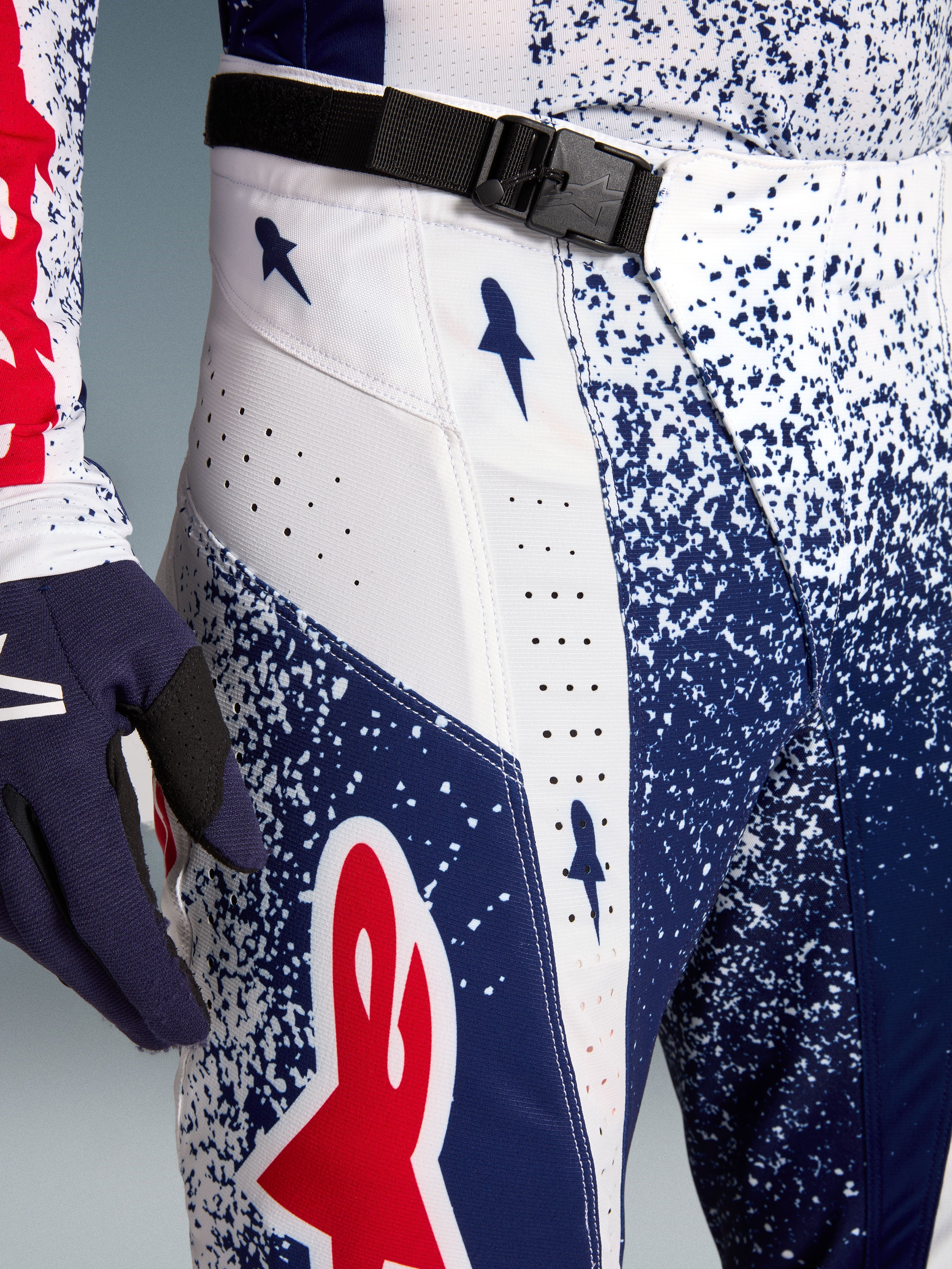 Alpinestars Techstar Unity Motocrosshose, blau-weiß gesprenkeltes Muster, rotes Logo und SX2-Magnetschnalle.
