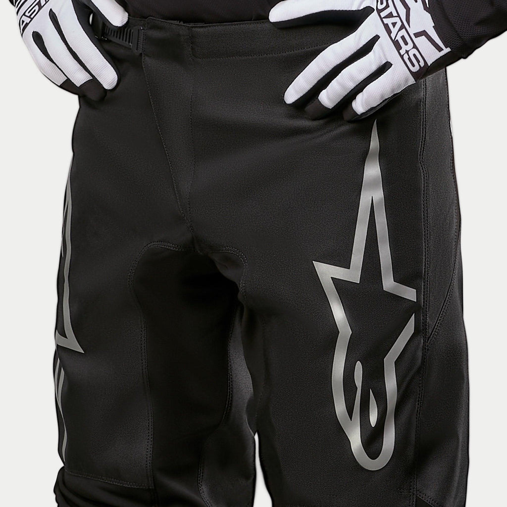 Alpinestars 2024 Fluid Graphite Pants, Motocross Pants, Black and Silver, detail shot of the upper thighs and waist, featuring a large silver star logo on the leg, worn with black and white racing gloves