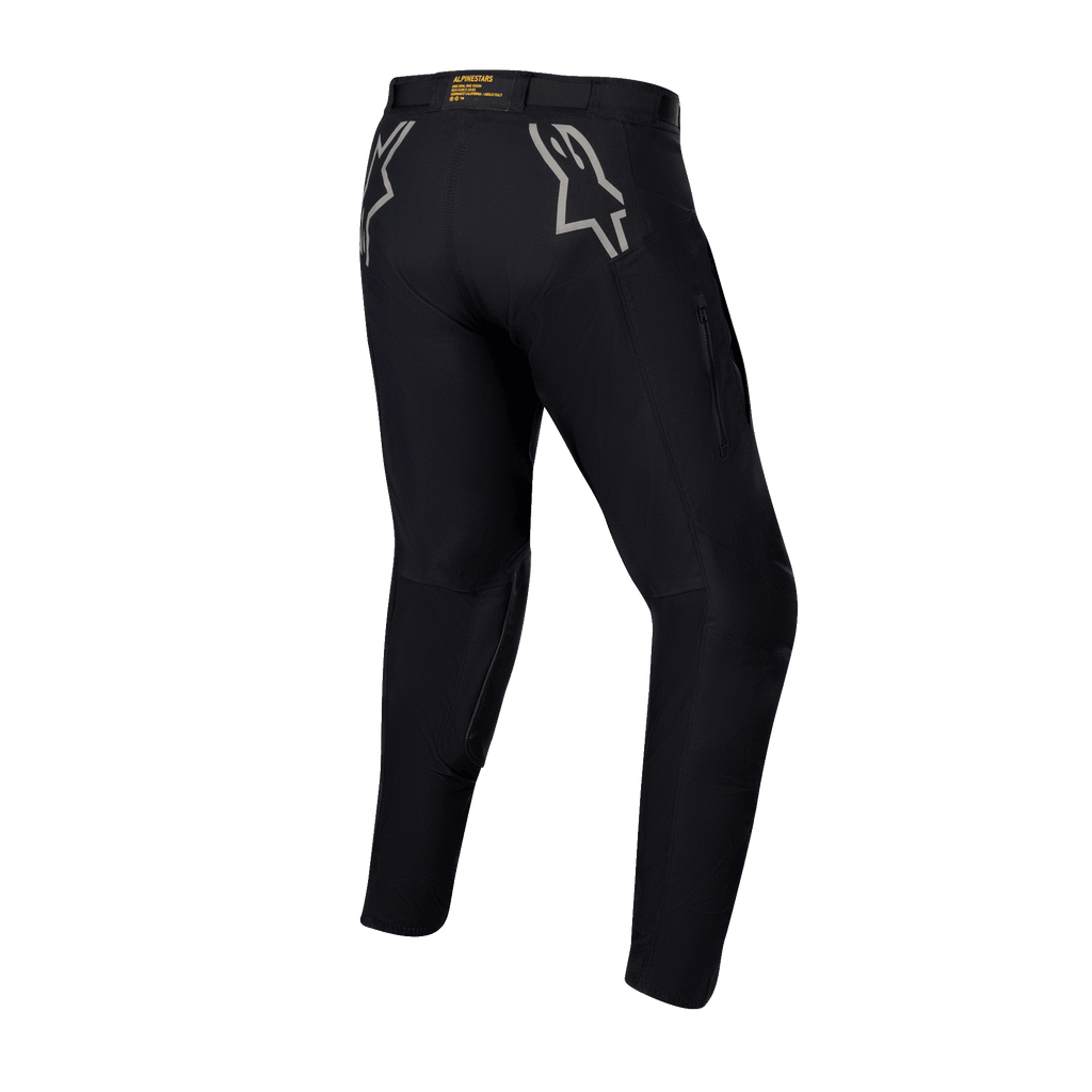 Alpinestars Techdura Hose, schwarze Enduro- und Offroad-Hose, Rückansicht mit grauen Stern-Logos auf den Hüften, gelbes Branding am hinteren Bund, robustes Stretch-Polyamid-Material mit strapazierfähigem Design für Motorradfahrten