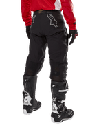 Alpinestars Techdura Hose, Offroad-Enduro-Hose, Schwarz, Rückansicht mit grauen Stern-Logos auf dem Gesäß, getragen mit einem roten langärmeligen Trikot und schwarz-weißen Tech 7 Stiefeln, robuste Textilkonstruktion für Abenteuerfahrten