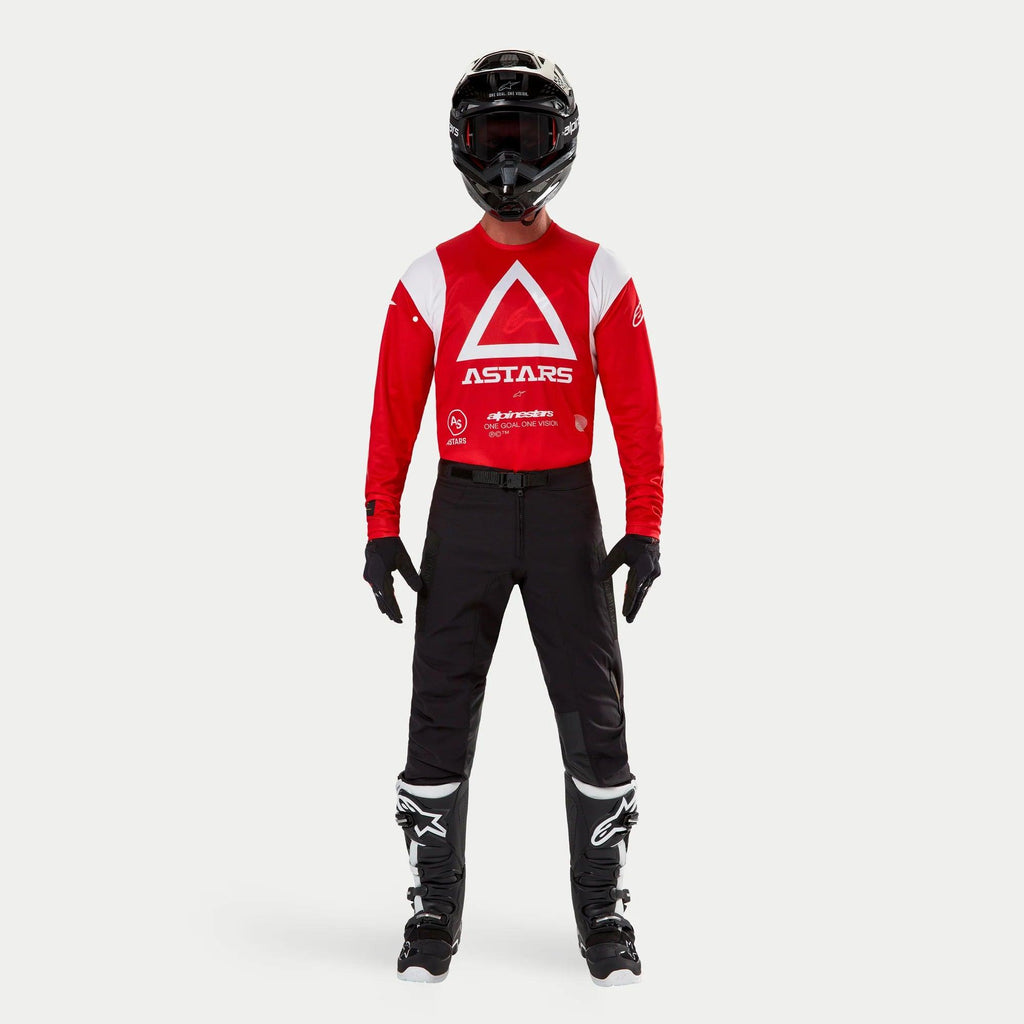 Alpinestars Techdura Hose, Enduro- und Offroad-Hose, Schwarz, kombiniert mit einem rot-weißen langärmeligen Astars-Trikot, schwarzem Helm und schwarz-weißen Stiefeln, mit robuster Stretch-Polyamid-Konstruktion und technischen Einsätzen für Offroad-Fahrten.