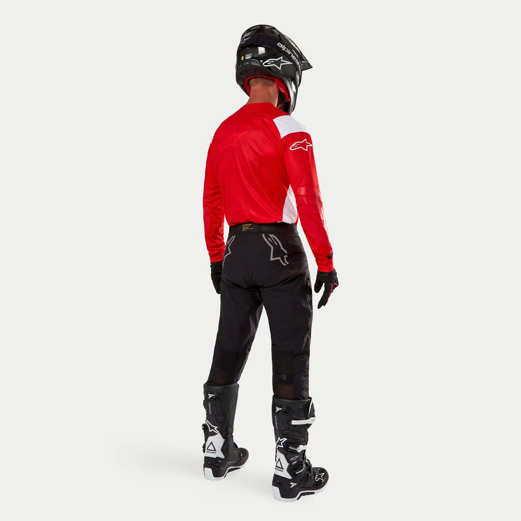 Alpinestars Techdura Hose, Enduro-Offroad-Hose, Schwarz, Rückansicht getragen von einem Fahrer mit einem rot-weißen Trikot und schwarz-weißen Stiefeln, mit weißen Stern-Logos auf der Rückseite und strapazierfähiger technischer Stretch-Konstruktion.