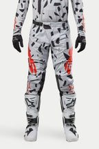 Alpinestars 2024 Techstar Rantera Hose, Motocross-Hose, Haze Gray Camo, getragen mit passendem Jersey, schwarzen Handschuhen und weißen Stiefeln, mit schwarzem Punktmuster und rotem Alpinestars-Branding, strapazierfähiges Design für den Offroad-Rennsport