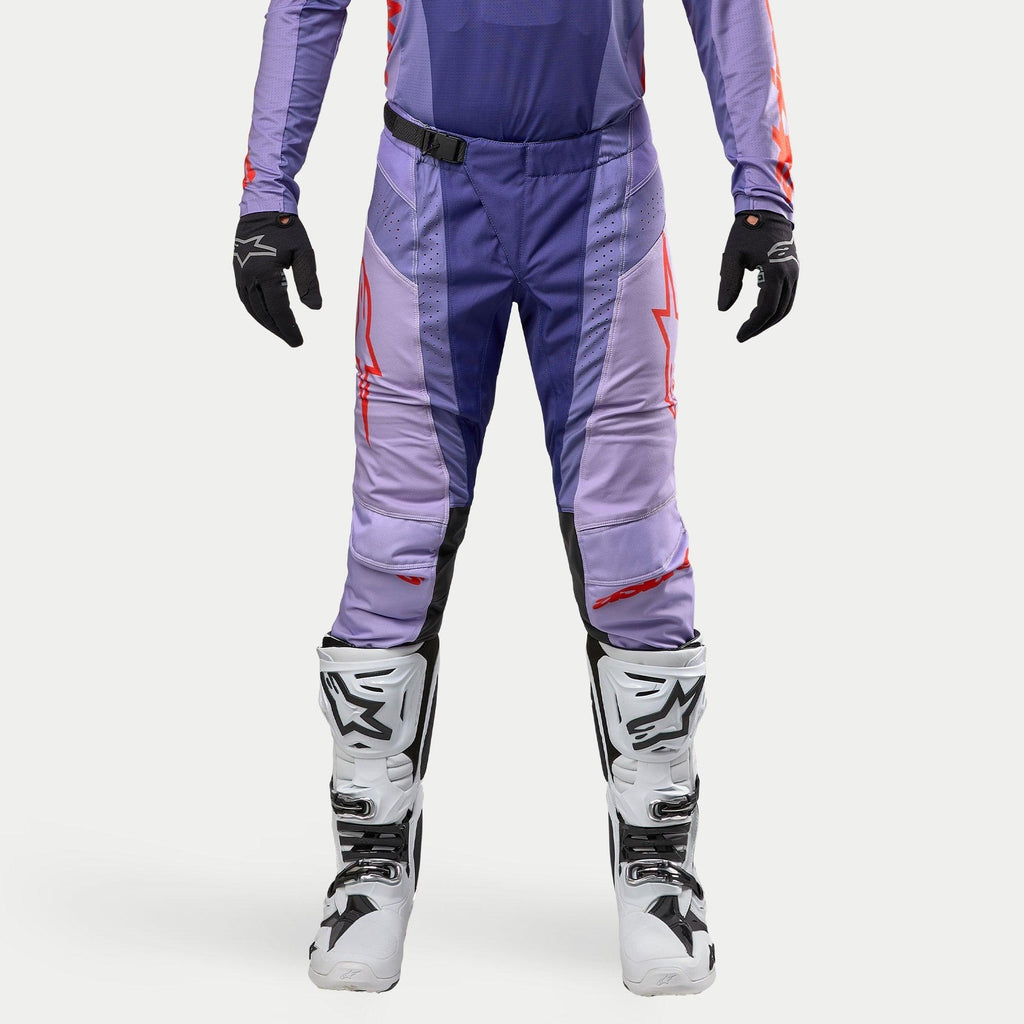 Alpinestars 2024 Techstar Ocuri Hose, Motocross-Hose in Lila und Hot Orange, strapazierfähiges Ripstop-Material, SX2 Magnetverschluss-Schnalle, Babel-Kniekonstruktion, kombiniert mit weißen Motocross-Stiefeln und schwarzen Handschuhen.