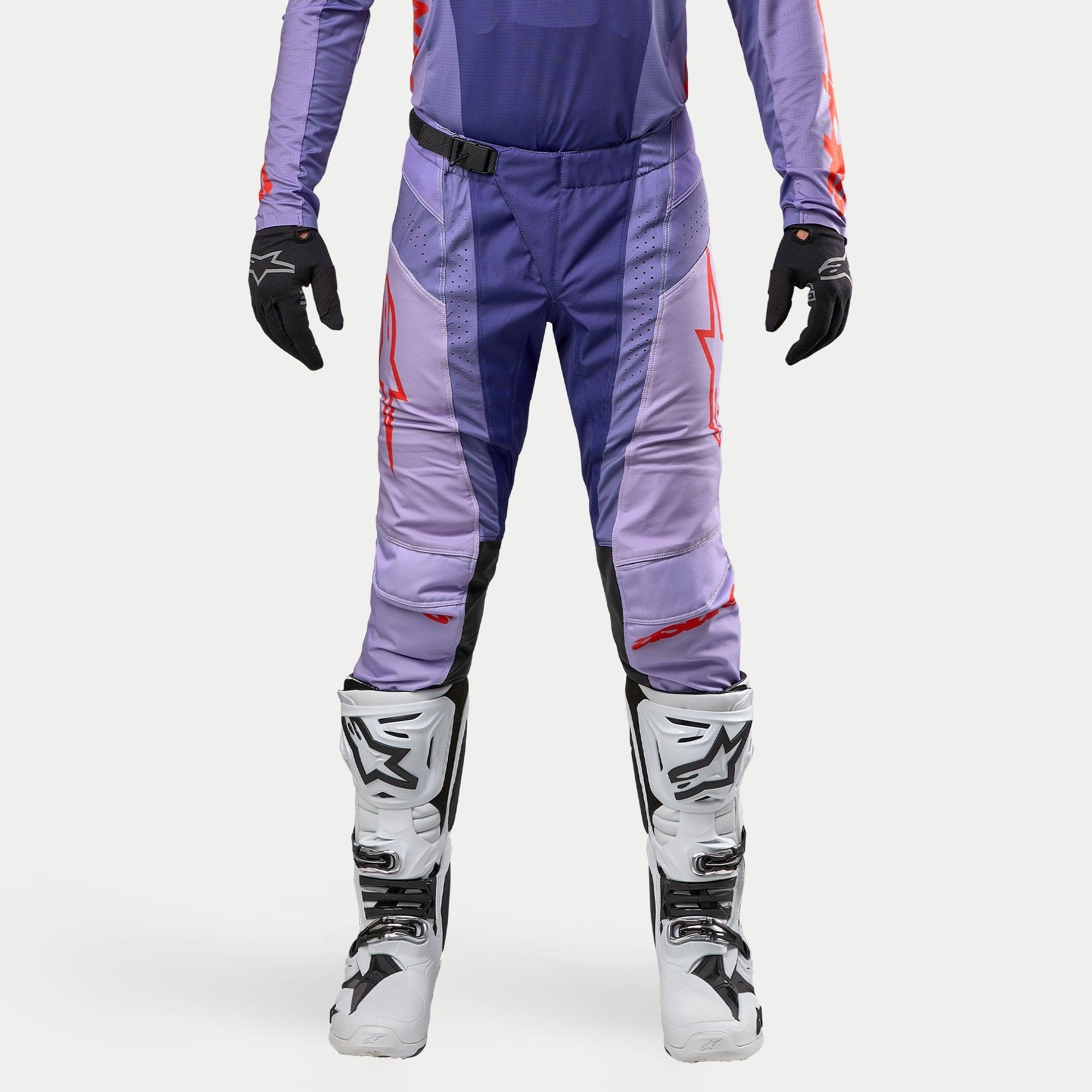 Alpinestars 2024 Techstar Ocuri Hose, Motocross-Hose in Lila und Hot Orange, strapazierfähiges Ripstop-Material, SX2 Magnetverschluss-Schnalle, Babel-Kniekonstruktion, kombiniert mit weißen Motocross-Stiefeln und schwarzen Handschuhen.