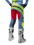 Alpinestars 2024 Techstar Ocuri Hose, Motocross-Hose, Hellblau, Gelb Fluo und Beerenrot, Rückansicht getragen mit weiß-schwarzen Motocross-Stiefeln, mit auffälligem Color-Blocking und markantem Alpinestars-Branding auf dem Gesäß.