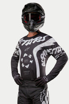 Alpinestars 2024 Racer Hana Jersey, Motocross Jersey, Black and White, featuring bold white Alpinestars text graphics and logo, worn by a rider with a black helmet and goggles, high-performance gear for off-road racing