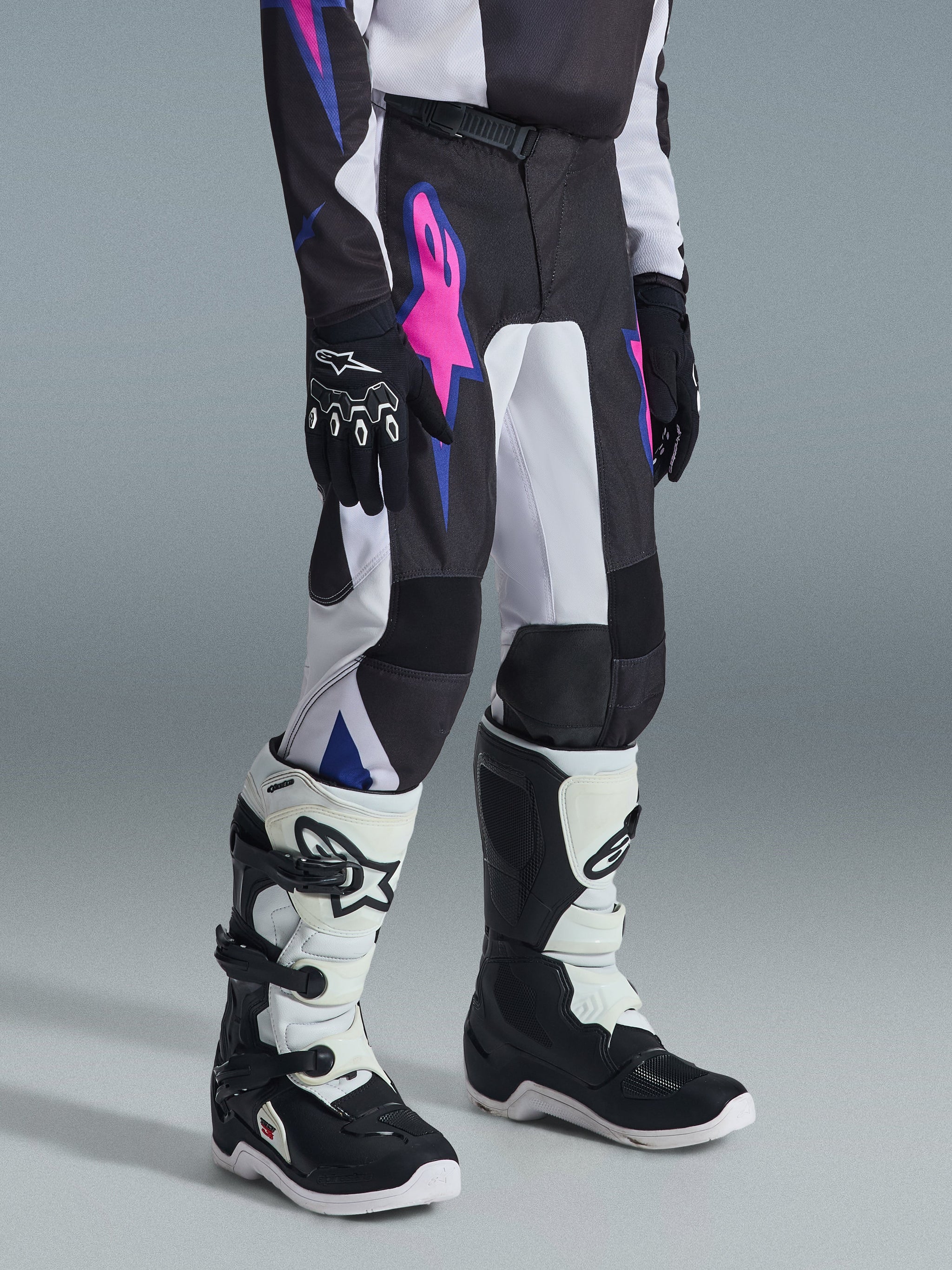 Alpinestars 2026 Youth Fluid Grid Pants, Motocross Pants, Black with white panels and vibrant pink and blue graphics, worn with matching black and white boots and black gloves, durable gear for youth off-road riding