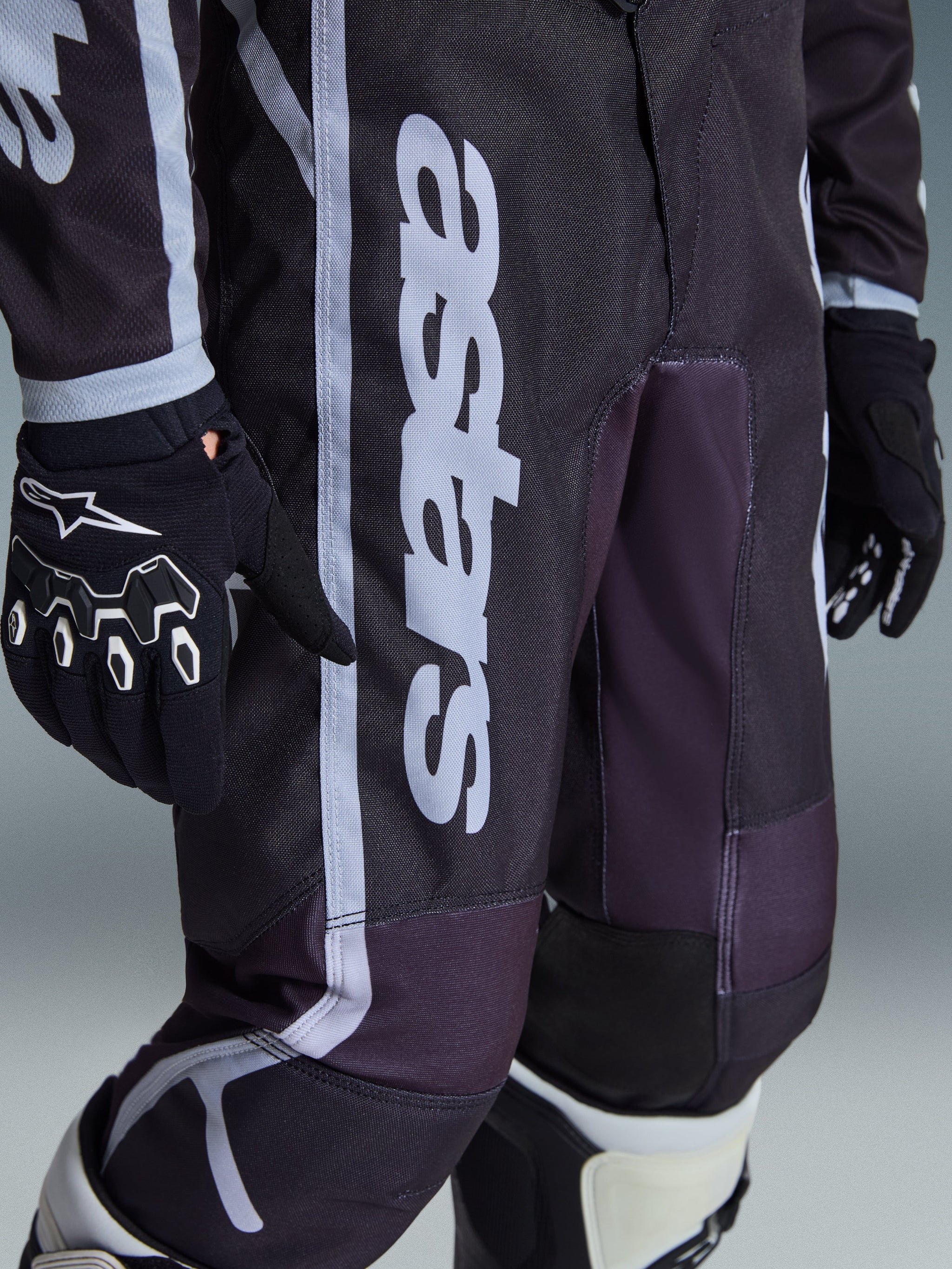 Alpinestars 2026 Youth Fluid Apex Hose, Motocross-Hose, Schwarz und Grau, Nahaufnahme mit weißem „astars“-Branding am Bein, getragen mit passenden schwarz-weißen Handschuhen und Stiefeln, sportliches Design für den Jugend-Offroad-Rennsport