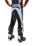 Alpinestars Jugend 2024 Racer Hoen Hose, Motocross-Hose, Hellgrau mit Akzenten in Hot Orange und Schwarz, Rückansicht mit schwarzen Einsätzen an Gesäß und Beinen, markantes Branding am hinteren Bund, getragen mit schwarz-weißen Motocross-Stiefeln für Offroad-Rennen