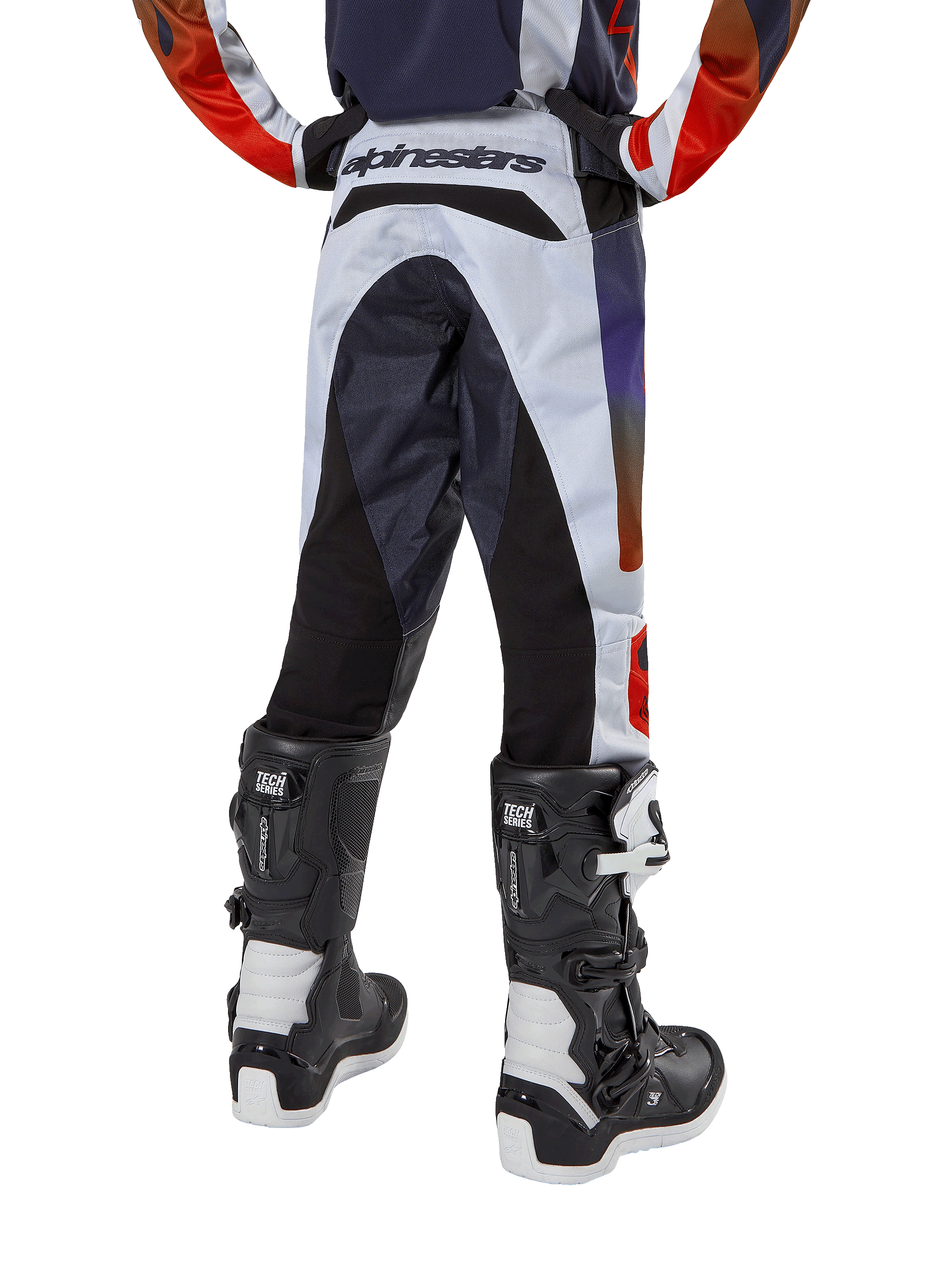 Alpinestars Jugend 2024 Racer Hoen Hose, Motocross-Hose, Hellgrau mit Akzenten in Hot Orange und Schwarz, Rückansicht mit schwarzen Einsätzen an Gesäß und Beinen, markantes Branding am hinteren Bund, getragen mit schwarz-weißen Motocross-Stiefeln für Offroad-Rennen