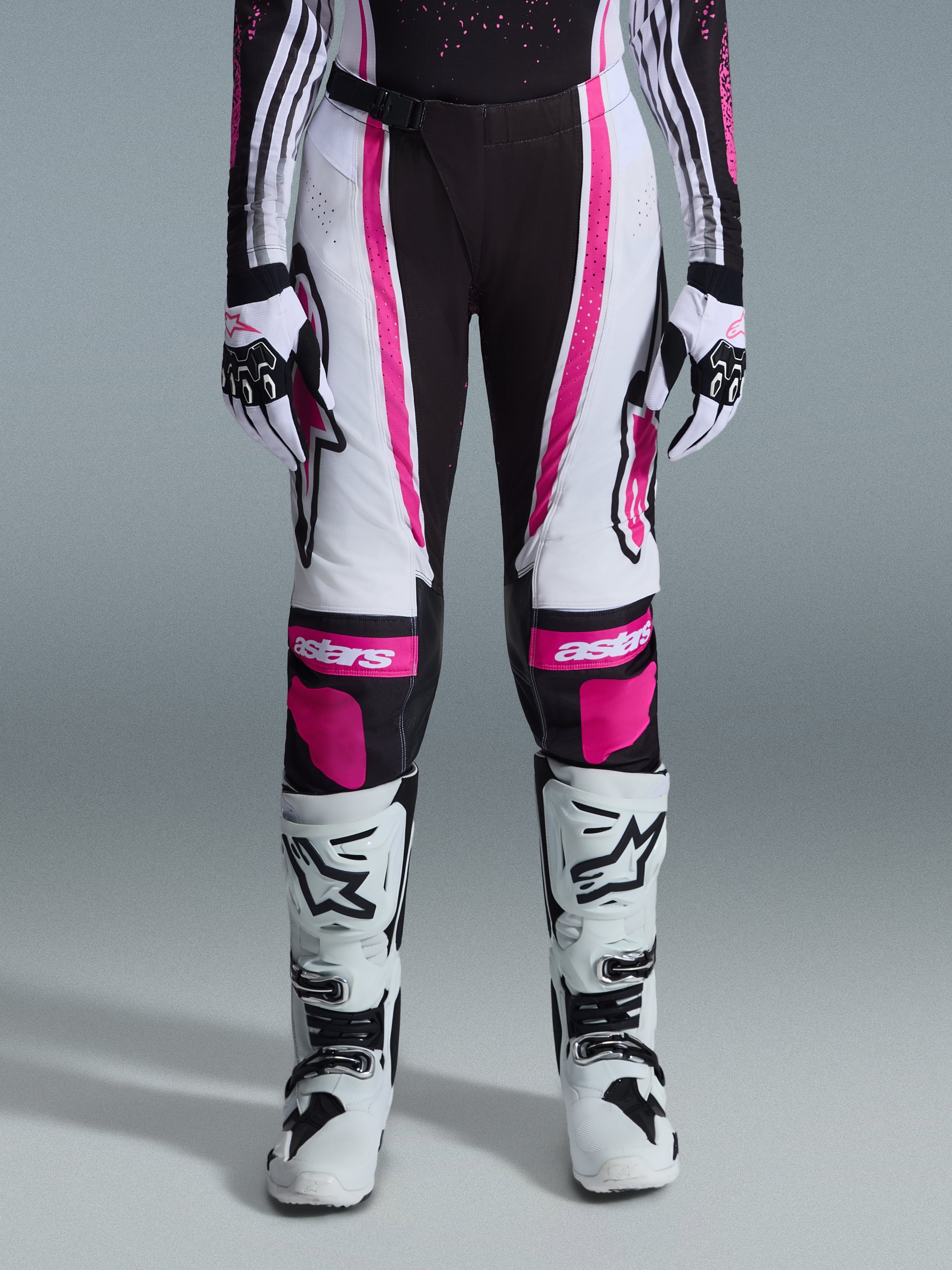 Alpinestars 2026 Stella Techstar Nomur Damen-Hose, Motocross-Hose, Schwarz, Weiß und Fuchsia, getragen mit passendem Renntrikot, Handschuhen und weißen Motocross-Stiefeln, mit auffälligen pinken Grafiken und Astars-Logos an den Knien, konzipiert für hochkarätigen Offroad-Wettbewerb.