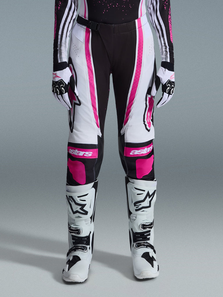 Alpinestars 2026 Stella Techstar Nomur Damen-Hose, Motocross-Hose, Schwarz, Weiß und Fuchsia, getragen mit passendem Renntrikot, Handschuhen und weißen Motocross-Stiefeln, mit auffälligen pinken Grafiken und Astars-Logos an den Knien, konzipiert für hochkarätigen Offroad-Wettbewerb.