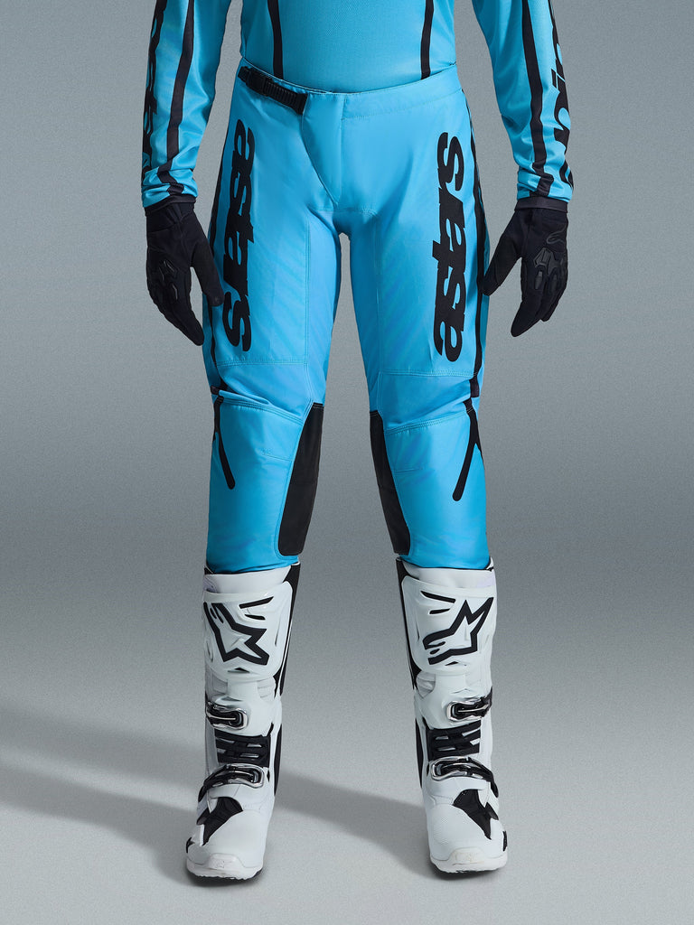 Alpinestars 2026 Stella Fluid Apex Damen-Hose, Motocross-Hose, Leuchtendes Cyan und Schwarz, vertikales schwarzes Branding auf den Oberschenkeln, schwarze verstärkte Knieinnenseiten, kombiniert mit weiß-schwarzen Motocross-Stiefeln und schwarzen Handschuhen, professionelle Offroad-Ausrüstung für Damen