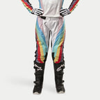 Alpinestars Stella Techstar Damen-Hose 2024, Motocross-Hose, Schwarz Mehrfarbig mit leuchtenden diagonalen Streifen in Weiß, Blau, Rot und Gelb, getragen mit schwarzen Motocross-Stiefeln und Handschuhen, renninspiriertes Design für Offroad-Performance.