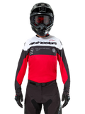 Alpinestars Pro-Dura Jersey, Motocross-Trikot, Schwarz, leuchtendes Rot und Weiß, getragen mit schwarzem Helm und Goggles, sportliches Design mit markantem Alpinestars-Branding und Laserperforationen, Performance-Enduro- und Offroad-Rennausrüstung