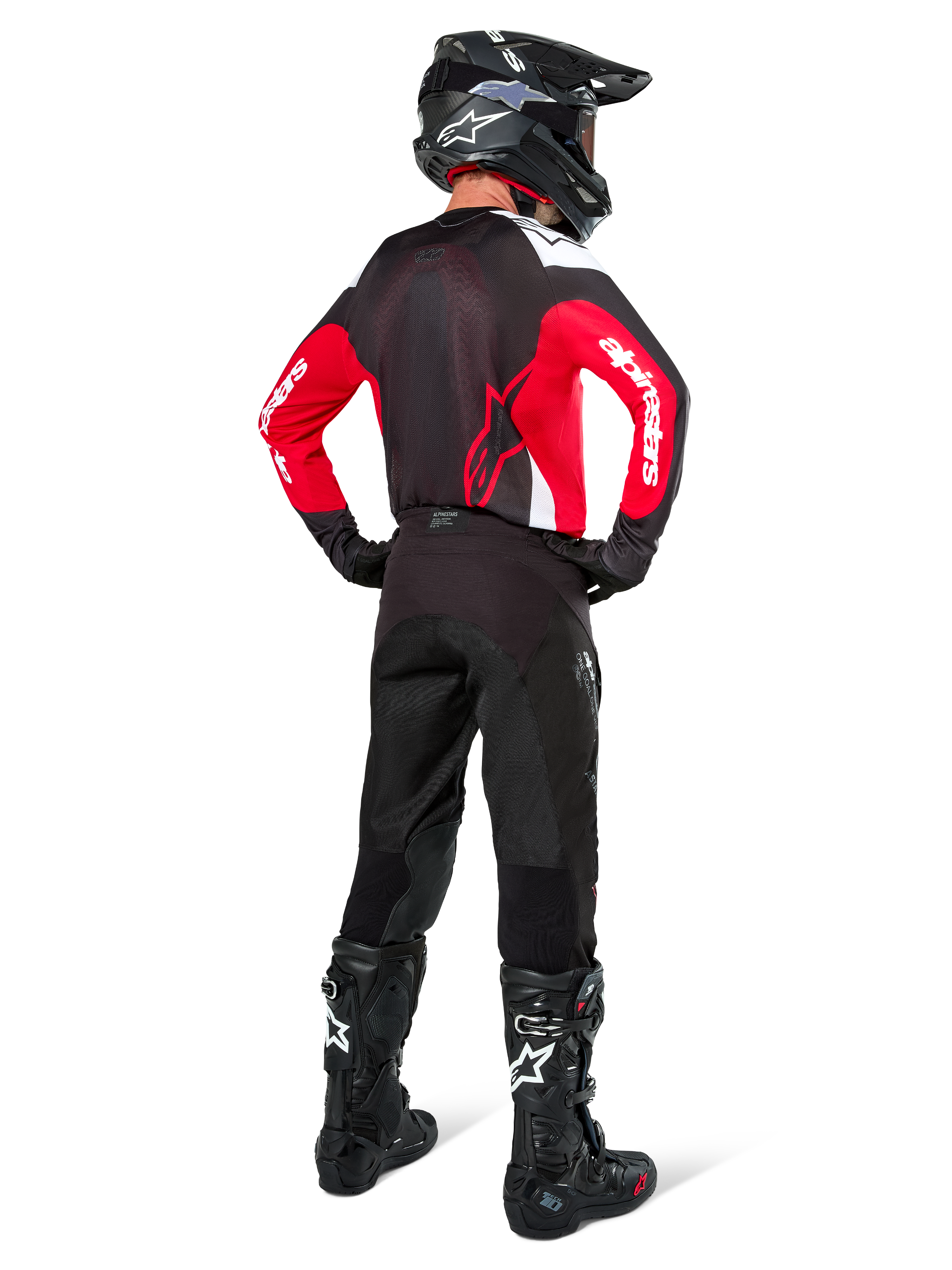 Motocross-Fahrer in der Rückansicht, Alpinestars Pro-Dura Jersey in Schwarz, Hellrot und Weiß, kombiniert mit schwarzer Motocross-Hose, Helm und Stiefeln, zeigt das Rückendesign und die Ärmellogos, abgestimmte Offroad-Rennausrüstung.