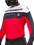 Alpinestars Pro-Dura Jersey, Motocross- und Enduro-Trikot, Schwarz, Leuchtend Rot und Weiß, mit „ONE GOAL. ONE VISION.“ Grafik und Laserperforationen auf der Brust, getragen mit schwarzer Motocross-Hose und Helm.