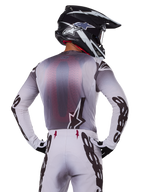 Motocross-Fahrer von hinten im Alpinestars 2025 Supertech Maker Trikot, Silber und Schwarz mit rotem Mesh-Rückeneinsatz und schwarzen Ärmellogos, kombiniert mit passender Motocross-Hose und einem schwarz-weißen Helm, professionelle Offroad-Rennausrüstung
