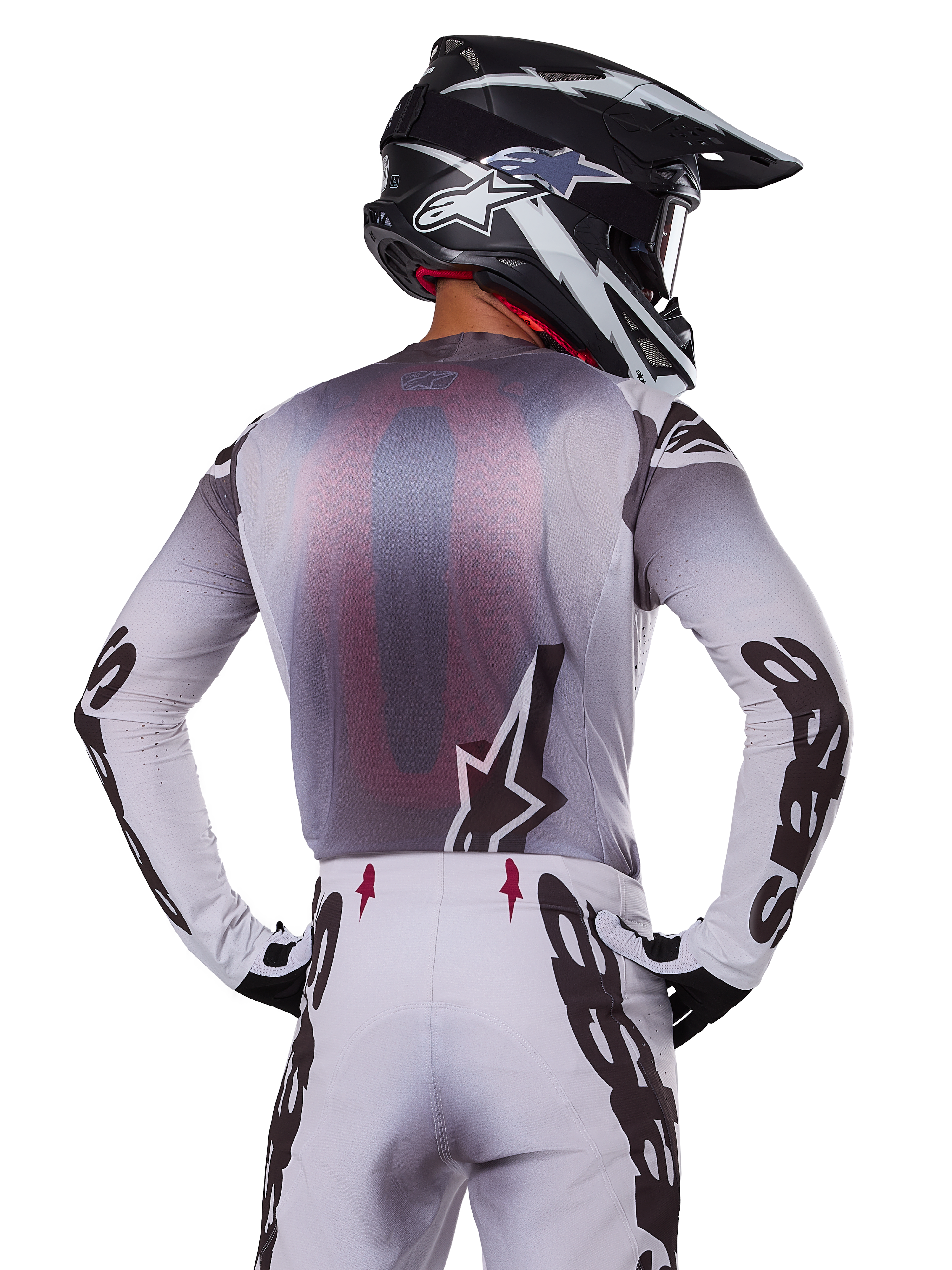 Motocross-Fahrer von hinten im Alpinestars 2025 Supertech Maker Trikot, Silber und Schwarz mit rotem Mesh-Rückeneinsatz und schwarzen Ärmellogos, kombiniert mit passender Motocross-Hose und einem schwarz-weißen Helm, professionelle Offroad-Rennausrüstung