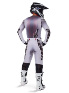Motocross-Fahrer von hinten in Alpinestars 2025 Supertech Maker Hose in Silber und Schwarz, passendes Langarm-Trikot, schwarz-weißer Helm und weiß-schwarze Stiefel, markantes schwarzes Branding an den Beinen, professionelle Offroad-Rennausrüstung
