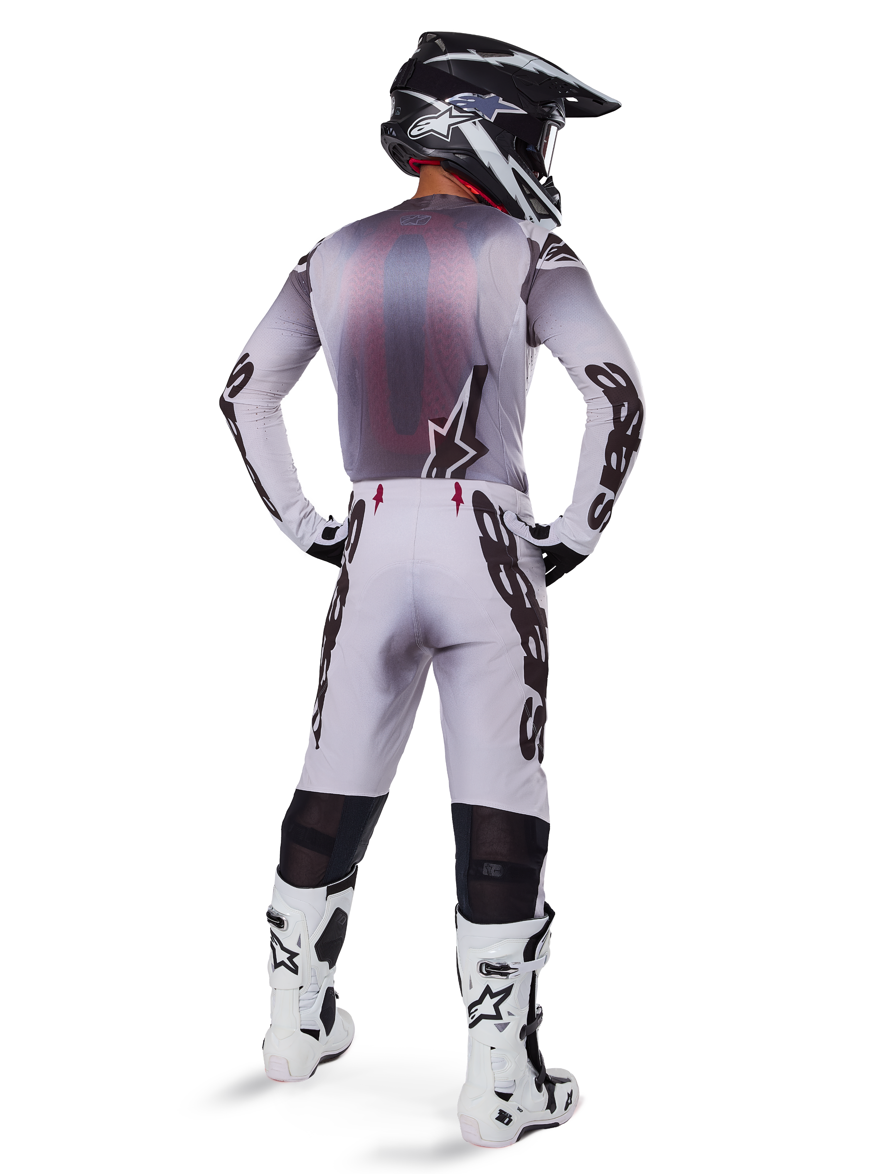 Motocross-Fahrer von hinten in Alpinestars 2025 Supertech Maker Hose in Silber und Schwarz, passendes Langarm-Trikot, schwarz-weißer Helm und weiß-schwarze Stiefel, markantes schwarzes Branding an den Beinen, professionelle Offroad-Rennausrüstung