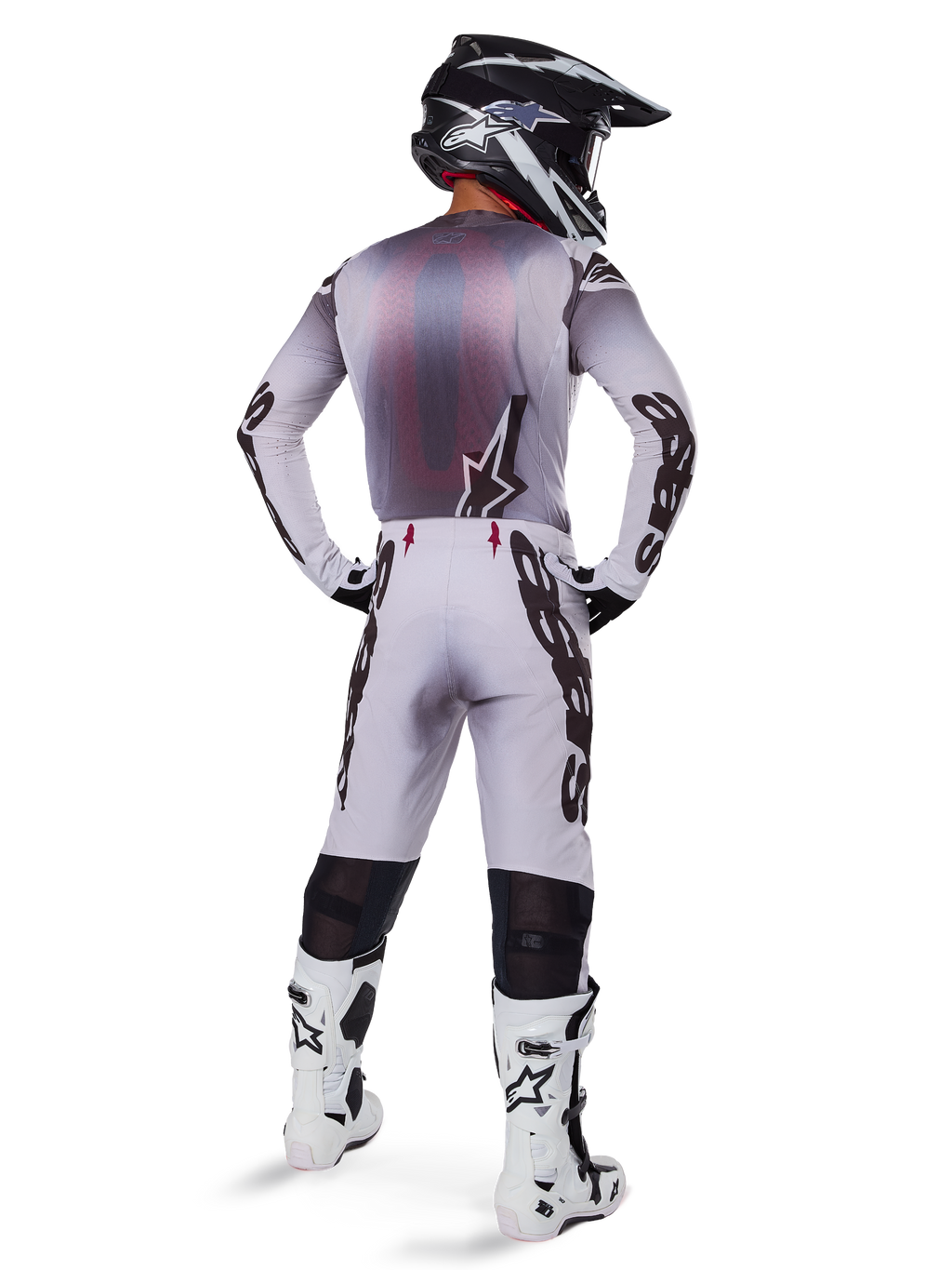 Alpinestars 2025 Supertech Maker Trikot, Motocross-Trikot, Silber und Schwarz, Rückansicht eines Fahrers in passender Ausrüstung und weißen Stiefeln, mit markantem Alpinestars-Branding auf den Ärmeln und einem Stern-Logo auf dem Rücken, athletische Race-Passform für professionelle Offroad-Performance.