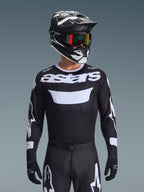 Alpinestars 2026 Racer Air Riway Jersey, Black and White motocross jersey with 'astars' branding, worn by a rider with matching black helmet, goggles, and pants, featuring breathable mesh panels for off-road racing.