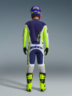 Motocross-Fahrer von hinten im Alpinestars 2026 Racer Air Riway Gear Set, blaues Trikot mit neongelben und hellgrauen Akzenten, weiß-blaue Hose mit neongelben Seiteneinsätzen, neongelbe Stiefel mit schwarzen Details, passender blau-gelber Helm, professionelle Ausrüstung für Offroad-Fahrten bei warmem Wetter