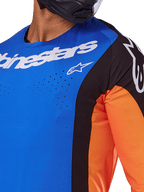 Alpinestars 2025 Techstar Melt Trikot, Motocross-Trikot, Blau und Orange mit schwarzen Einsätzen, weißes Alpinestars-Branding und sichtbare lasergeschnittene Perforationen auf der Brust, getragen von einem Fahrer mit schwarzem Helm