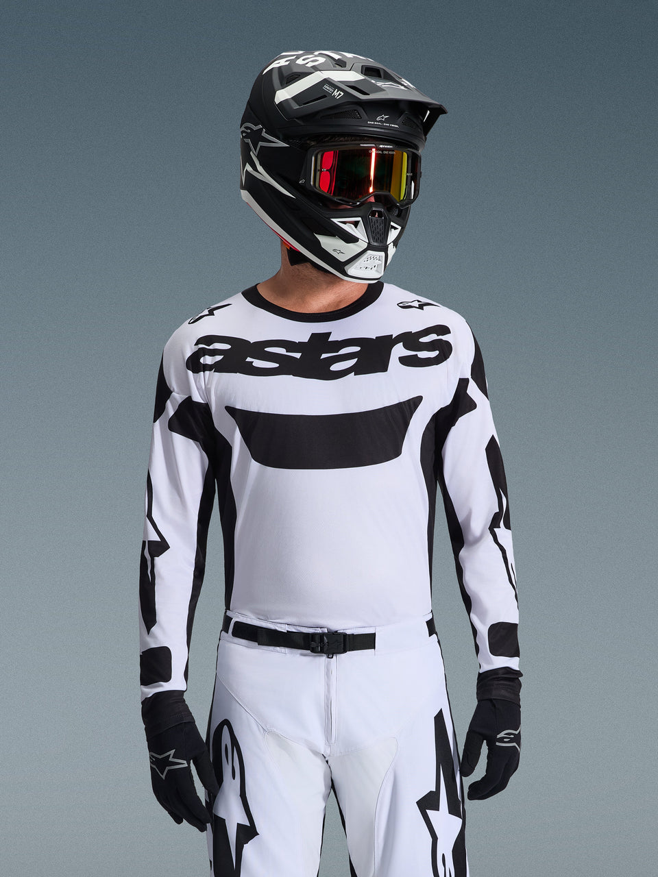 Motocross-Fahrer im Alpinestars 2026 Racer Riway Trikot in Weiß und Schwarz, mit 'astars'-Branding auf der Brust, kombiniert mit passender weiß-schwarzer Hose, schwarzem Helm mit Goggles und schwarzen Handschuhen, abgestimmte Ausrüstung für den Offroad-Rennsport