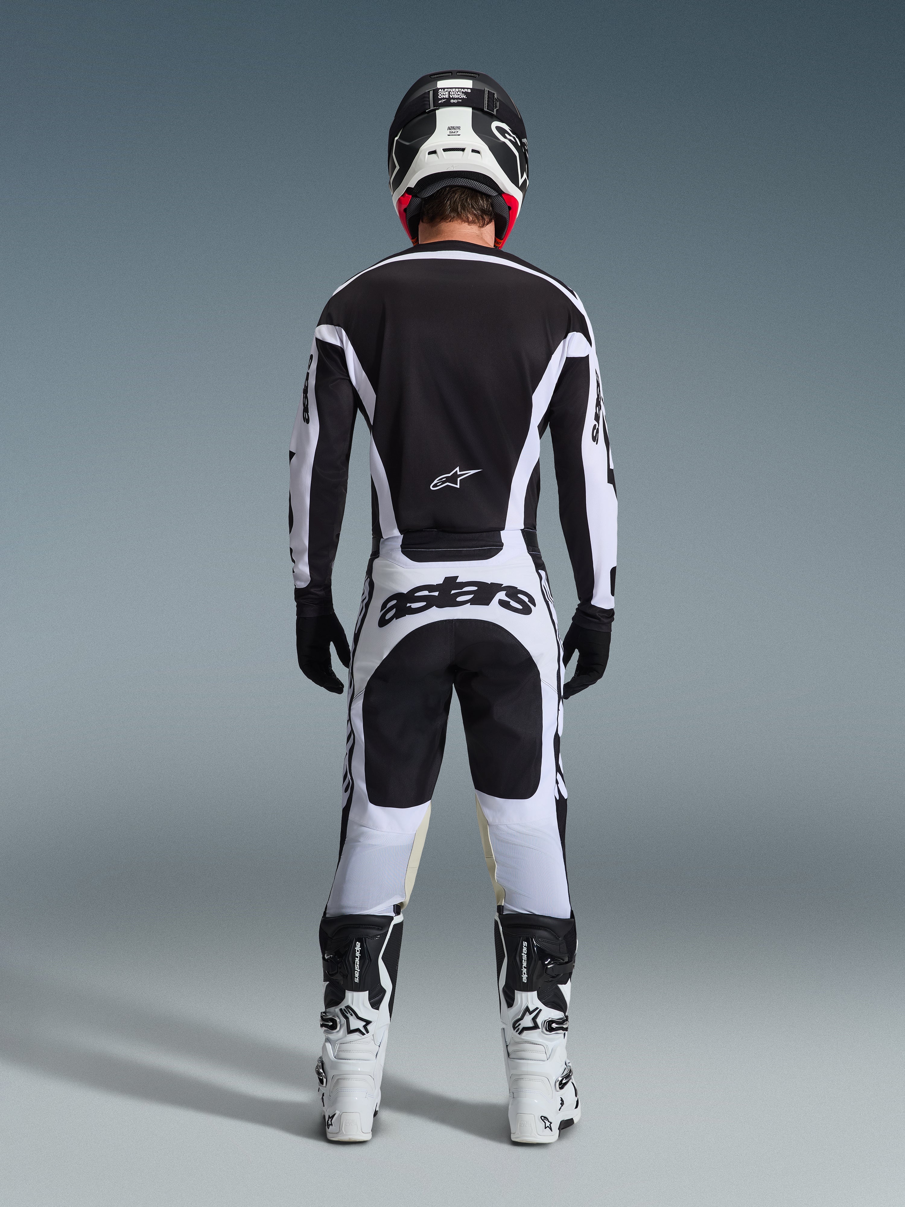Motocross rider from the back wearing complete racing gear, 2026 Racer Riway Jersey in White and Black, matching pants with 'astars' branding on the seat, black helmet with white details, black gloves, and white and black boots, coordinated professional off-road outfit