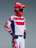 Motocross-Fahrer im Alpinestars 2026 Racer Riway Trikot in Weiß Blau Rot, mit markantem rotem „astars“-Branding auf der Brust und blauen Seiteneinsätzen, kombiniert mit einem passenden roten Helm und einer weißen Rennhose für einen kompletten Offroad-Performance-Look.